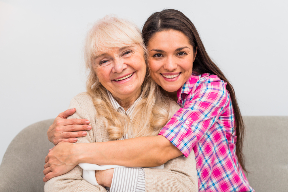 A portrait of a smiling young woman hugging an older senior woman, likely her mother or grandmother.