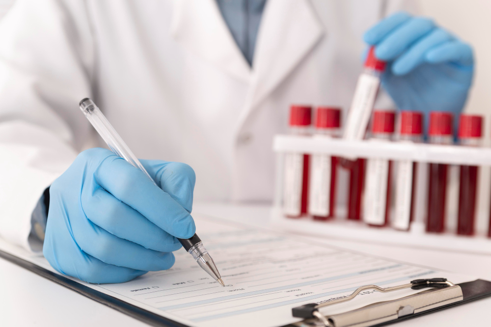 A medical professional in blue gloves writing on a form while handling a test tube containing a blood sample.