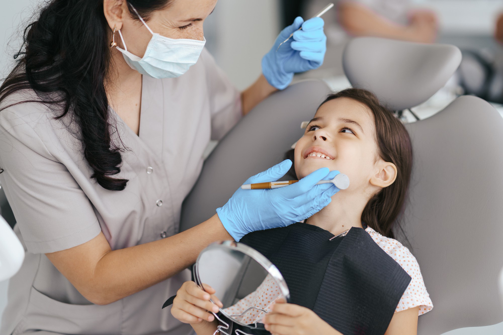 A young girl holding a hand mirror and smiling at a female dentist during a dental check-up.